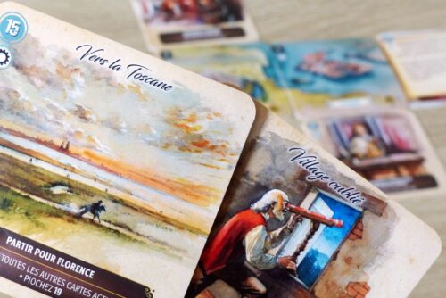 "Boîte de jeu CARTAVENTURA : COSMOLOGIA posée sur une table en bois, entourée de cartes illustrées représentant des scènes historiques et fantastiques."